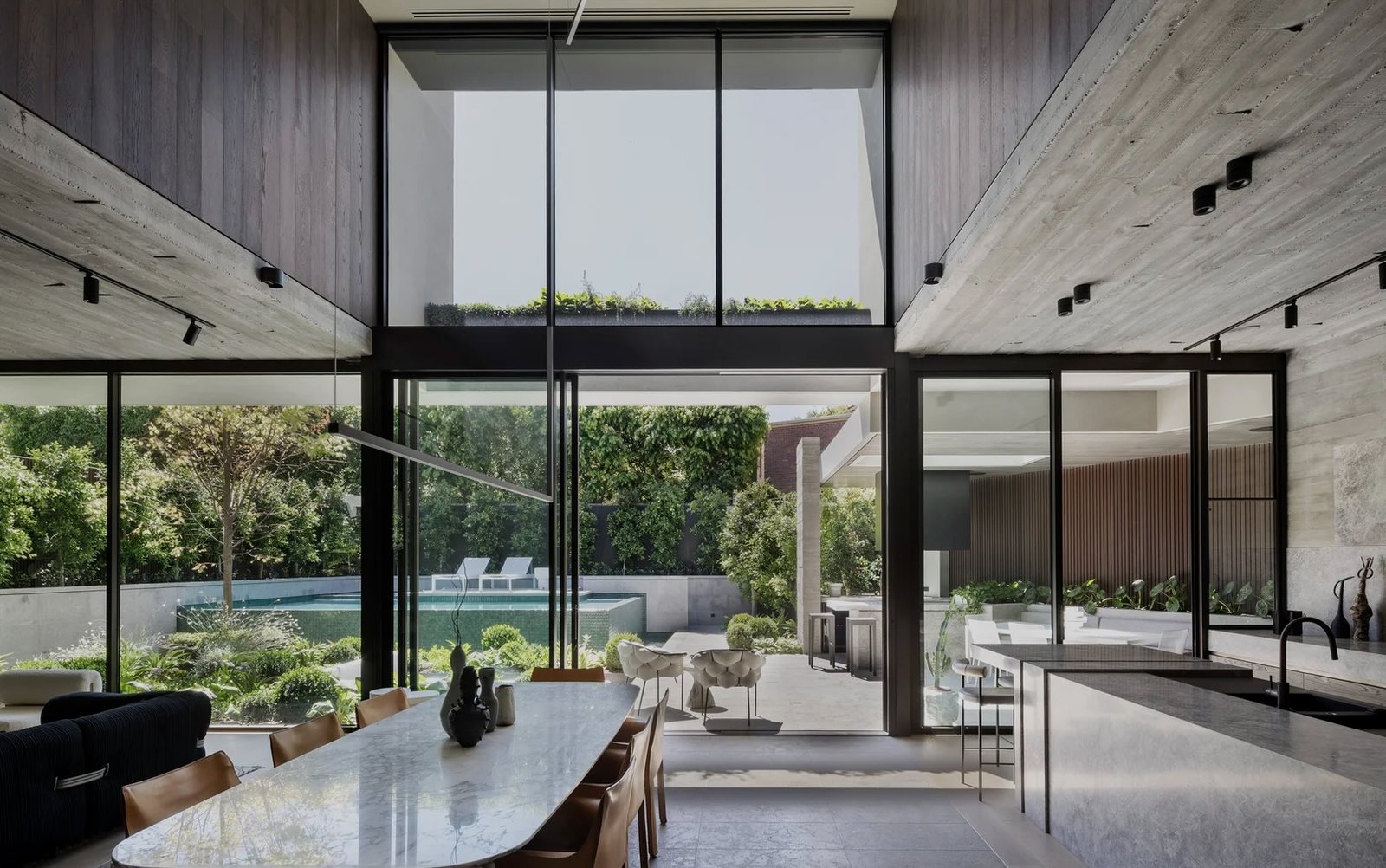 Double-height dining and kitchen space with floor-to-ceiling glazing opening to the pool, Melbourne